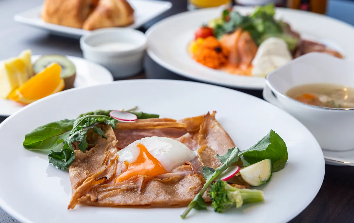A breakfast plate featuring a thin pancake topped with a soft-boiled egg and ham.