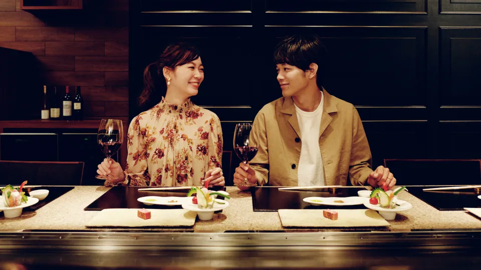 A man and a woman enjoying wine at a teppanyaki counter.