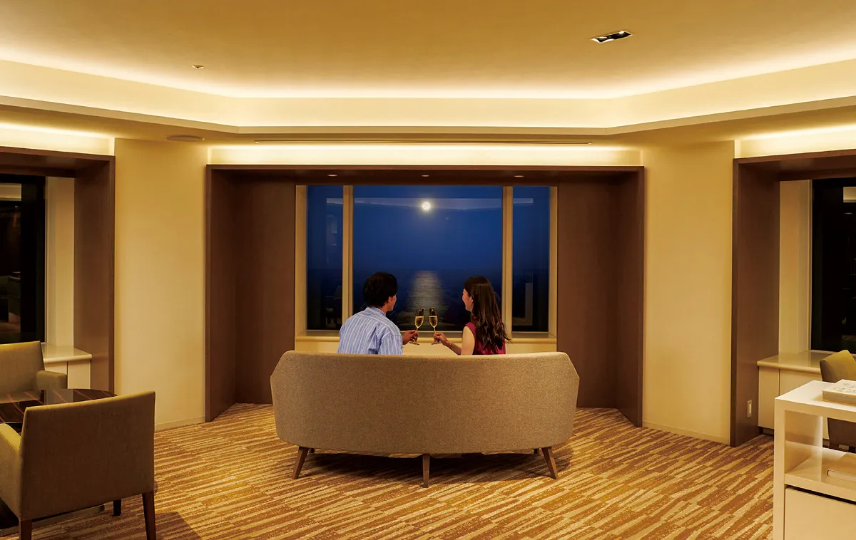 A man and a woman gaze at the moonlit sea from the club lounge.